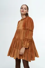 Vestido corto de terciopelo color cobre, con diseño de volados en capas, cuello redondo con detalle de volado y mangas largas con fruncidos.
