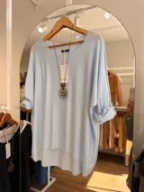 Sweater de tejido fino y suave con diseño oversize, cuello redondo y mangas largas con puños arremangados. Presenta un corte asimétrico con el ruedo trasero más largo que el delantero y bordes sin costuras visibles.