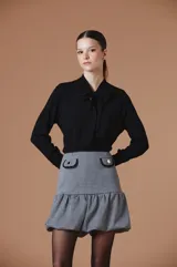 Falda corta con estampado pied de poule, diseño de corte balloon con volado en el ruedo que aporta volumen y movimiento. Presenta una silueta estructurada con detalle de tapitas decorativas en la cintura.