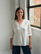 Blusa blanca de manga larga con cuello en V y cierre frontal de botones. Presenta una textura sutil en la tela y un corte recto y holgado.