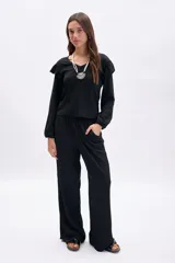 Pantalón negro de tiro alto con cintura elástica y corte ancho (wide leg). Presenta una textura sutil en la tela y bolsillos laterales.