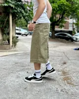 Bermuda de corte baggy color verde con efecto gastado. Presenta costura vertical trasera en cada pierna y detalle artesanal visible en el bajo. Incluye un cordón extra confeccionado en la misma tela.