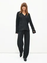 Camisa negra con textura plisada, cuello clásico, escote en V y mangas largas.