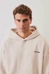 Hoodie de felpa color beige, con capucha, bolsillo frontal tipo canguro y pequeño logo de la marca estampado en el pecho.