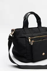 Cartera negra de nylon con diseño compacto y funcional. Cuenta con asas cortas y correa regulable desmontable para llevar al hombro o cruzada, además de múltiples bolsillos con cierre y detalles dorados.