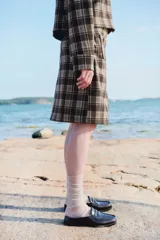 Pollera de tiro alto a la rodilla confeccionada en punto bondeado con diseño a cuadros en tonos marrón y beige. Presenta dos bolsillos de parche frontales con botones metálicos dorados, cierre oculto posterior y bajo recto.