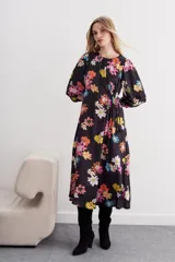 Vestido midi negro con estampado de flores grandes y coloridas (rosado, naranja, amarillo, blanco, azul). Presenta mangas balloon, escote redondo con tablas y ajuste en la cintura con lazo.