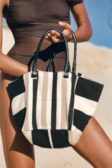 Bolso tipo shopper de algodón con diseño de rayas en tonos negro, blanco y beige. Cuenta con asas de mano de piel negra, forro interior con bolsillo y cierre magnético.