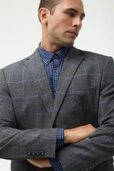 Blazer de corte sastre en color gris con estampado de cuadros en tonos azules. Presenta cierre frontal de dos botones, solapas clásicas y bolsillos laterales con solapa.