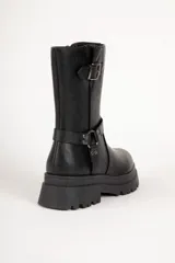 Bota biker negra de símil cuero, con punta redonda y apliques de tachas, hebilla y argolla. Plataforma tractor de 5cm y cierre lateral.