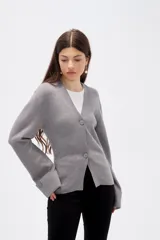 Saco de punto gris con cuello en V, cierre frontal con botones y mangas largas con puños anchos decorados con botones.