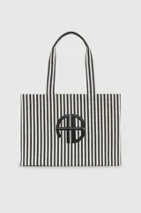 Bolso tipo shopper de diseño rectangular y amplio, confeccionado en tela con patrón de rayas verticales en color blanco y negro. Cuenta con dos asas superiores para llevar al hombro y detalle de aplique metálico con monograma en el centro.