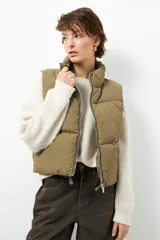 Chaleco puffer color beige, sin mangas, con cuello alto y cierre frontal con cremallera.