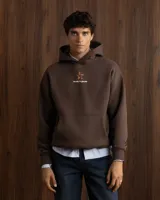 Hoodie de algodón color marrón con capucha y estampado gráfico en la espalda que incluye texto y logo de la marca.