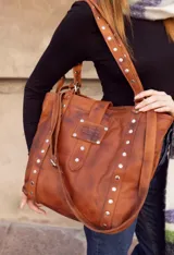 Bolso tipo tote bag de cuero negro con apliques metálicos plateados.