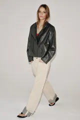 Chaqueta de corte amplio estilo biker en tejido efecto piel de color verde oscuro, con cuello alto envolvente, cierre frontal asimétrico de cremallera metálica, bolsillos ocultos en costura y forro interior.