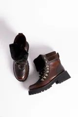 Borcegos de cuero vacuno en tonos marrón, con diseño de caña media y cuello con forro de piel sintética negra. Presentan cordones marrones, ganchos metálicos para ajuste y suela de goma tipo track con plataforma.