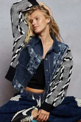 Campera de jean color negro con cuerpo de denim desgastado y mangas tejidas en contraste con diseño geométrico en blanco y negro. Presenta cuello camisero, cierre frontal con botones metálicos y detalles de desflecado en las costuras.