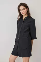 Camisa negra de manga corta, con cuello camisero, cierre frontal de botones y un bolsillo aplicado en el pecho.
