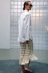 Falda midi de punto crochet en color crudo, con diseño de red, cintura elástica y bajo terminado en flecos largos.