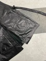 Chaleco de cuero negro, abierto a los costados, con tiras que se regulan a necesidad y gusto de cada una. Presenta bolsillos frontales y escote en V.