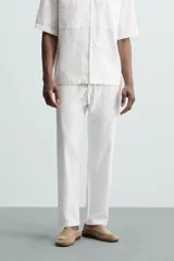 Pantalón de corte relajado color beige confeccionado en tejido de mezcla de algodón y lino. Posee cintura elástica ajustable con cordón, bolsillos frontales y bolsillos traseros de vivo.