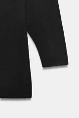 Vestido corto de punto negro confeccionado en mezcla de viscosa, con cuello barco, manga larga y detalle de costuras marcadas.