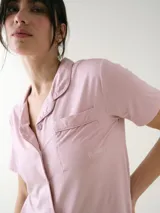 Camisa de manga corta para dormir de color rosado, confeccionada en viscosa. Presenta botones frontales, cuello con solapa, bolsillo en el pecho y ribetes a tono.