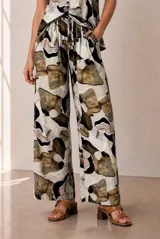 Pantalón de corte ancho, tiro medio, con cintura elástica ajustable mediante cordón y bolsillos laterales, con diseño estampado de pétalos en tonos beige, marrón y negro.