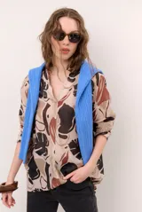 Blusa de manga larga con estampado abstracto de hojas en tonos beige, marrón y negro, con cuello en V y cierre frontal con botones ocultos.