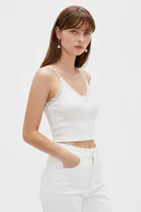 Musculosa de punto blanco, corte crop, con tirantes finos, escote en V adornado con detalles de encaje y un pequeño lazo en el centro.