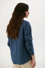 Sobrecamisa de lino en color azul, con diseño de corte recto, cuello camisero, cierre frontal con botones oscuros y detalle de cinta en contraste a lo largo de la botonadura. Cuenta con bolsillos frontales con solapa y costuras visibles en color claro.