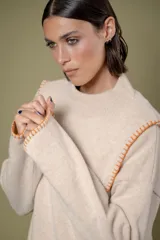 Buzo de lana color beige con cuello redondo y costuras decorativas bordadas en color naranja a lo largo de los laterales y puños. Presenta un diseño holgado y mangas largas.