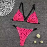 Bikini de dos piezas con estampado de corazones pequeños sobre fondo fucsia. La parte superior es de estilo triángulo con tiras negras, y la parte inferior es de corte tanga con tiro alto.