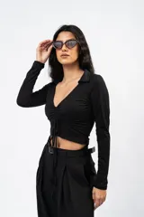 Crop top negro de manga larga con cuello polo, escote en V y detalle de frunce central ajustable con cordones.