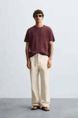 Pantalón de corte recto, color beige claro, con pliegues frontales y bolsillos de vivo en la parte trasera.