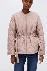 Campera acolchada de nylon guateado en color rosado, con cuello redondo, cierre frontal y cordón ajustable en la cintura con tiras colgantes. Presenta diseño acolchado con patrón de rombos, mangas largas y hombros caídos.