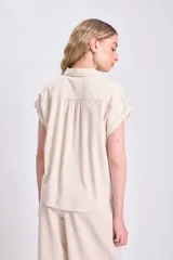 Camisa casual de lino color crudo, con cuello camisero, manga corta doblada y cierre frontal con botones oscuros.