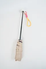 Paraguas plegable de color beige con la palabra 'hello.' estampada en color verde. Incluye una correa de muñeca de color amarillo con detalles en fucsia.