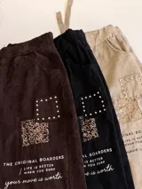 Pantalón de corte relajado color beige, con cintura elástica y cordón ajustable. Presenta parches decorativos con lentejuelas y tachas en los muslos, además de detalles de texto estampado. Posee bolsillos laterales y dobladillo en los tobillos.