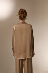 Camisa de poliéster con acabado satinado, de corte holgado, cuello camisero clásico, cierre frontal con botones y mangas largas con puños.