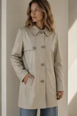 Trench de cuero ovino color cemento, de diseño clásico con solapa en el pecho, bolsillos laterales ojal y cierre frontal con botones.