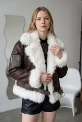 Campera tipo aviador de ecocuero color chocolate, con interior y bordes de piel sintética blanca. Presenta cierre frontal, bolsillo con cierre en la manga derecha y cinturón ajustable en la parte inferior.