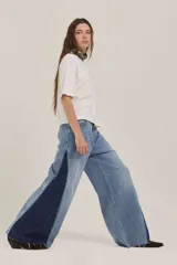 Pantalón de jean de corte wide leg con diseño bicolor, combinando un tono de denim claro en el frente y un panel lateral en denim azul oscuro. Presenta un acabado deshilachado en el ruedo.