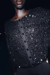 Chaqueta de punto negra con lentejuelas brillantes, cuello redondo, manga larga y cierre frontal con botones.