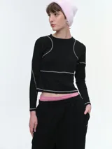 Remera de manga larga confeccionada en tela waffle color negro, con costuras decorativas en contraste de color blanco. Presenta cuello redondo y un corte ligeramente cropped.