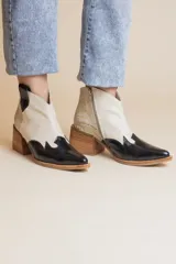 Bota corta de cuero color blanco y negro con detalle de textura simil piel de cocodrilo en el talón. Tiene cierre lateral y taco de madera.