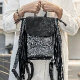 Mochila negra de cuero vacuno con textura tipo piel de cocodrilo, tapa de gamuza con cierre a presión y flecos laterales.