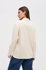 Remera tipo polo de manga larga en color beige, confeccionada en algodón pesado con textura suave. Presenta cuello clásico, cierre frontal con botones y un pequeño bordado en el pecho. Posee puños en las mangas y un corte relajado.