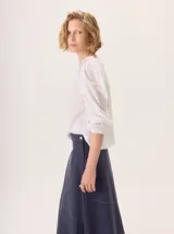 Camisa blanca de manga larga con volados en los hombros y puños ajustados con elástico. El cuerpo es de tejido de punto y las mangas y el delantero son de tejido de camisa.